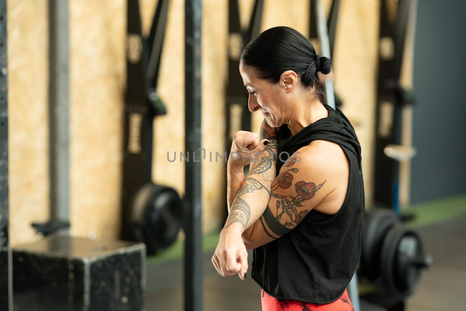 Side view of a mature strong woman with tattoos warming up in a cross training center