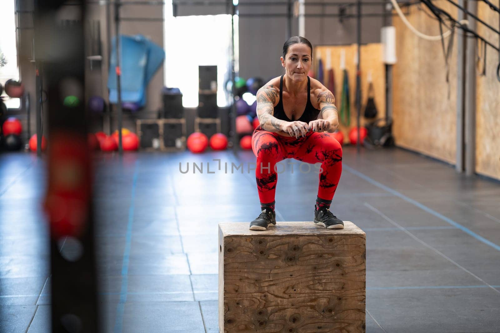 Strong tattooed woman jumping on a box in a cross training center