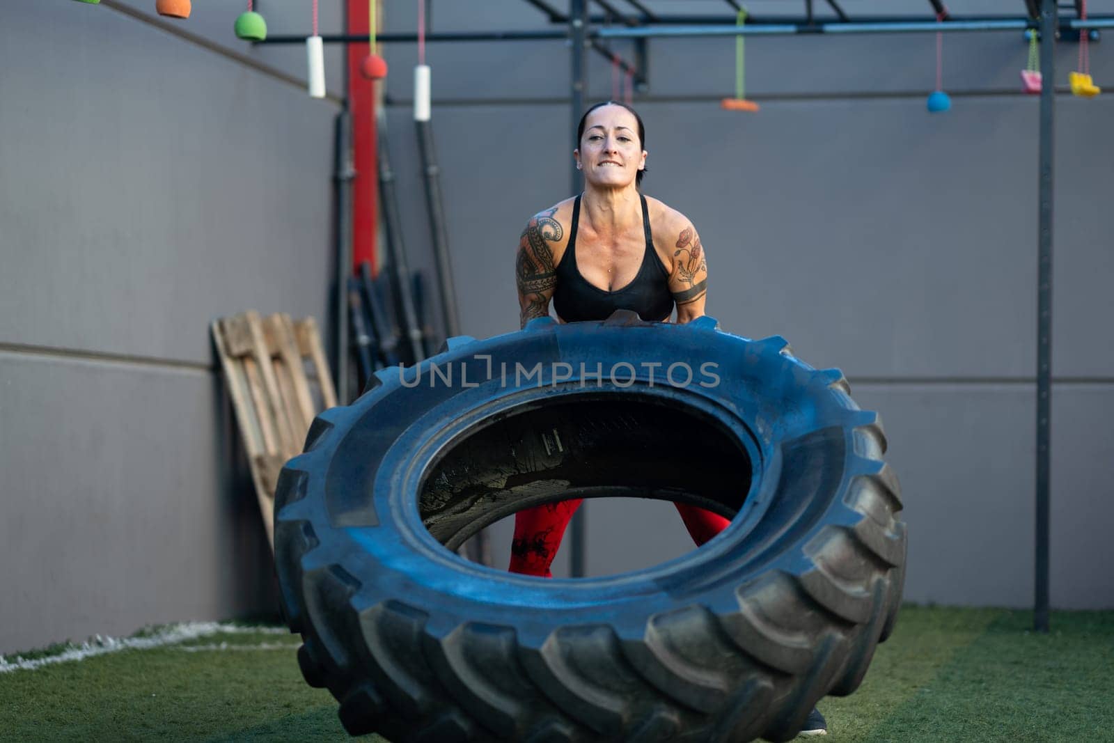 Strong mature woman lifting a wheel in a gym by javiindy