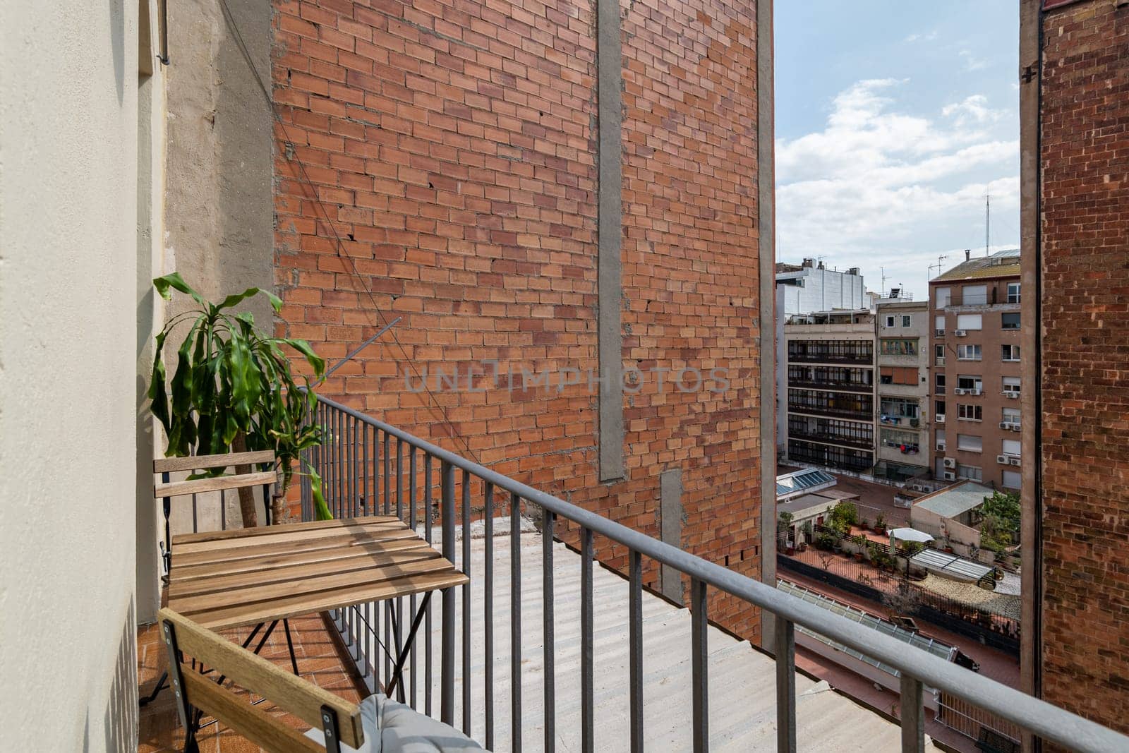View from the terrace to the courtyard of a multi-storey new building complex on a sunny summer day. Table and chair on an open balcony in a new building by apavlin
