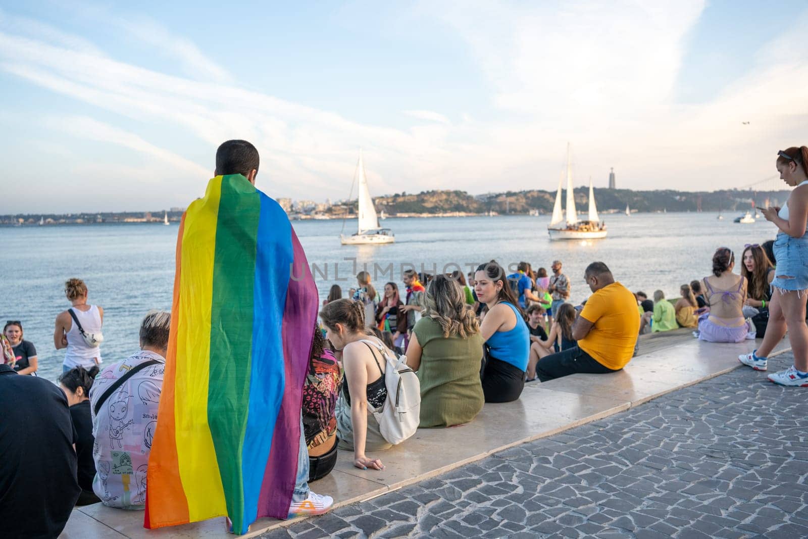 Lisbon, Portugal. 17 June 2023: Friends walking along Lisbon's promenade during Pride Parade. Cheerful happy free young people with rainbow flags and posters