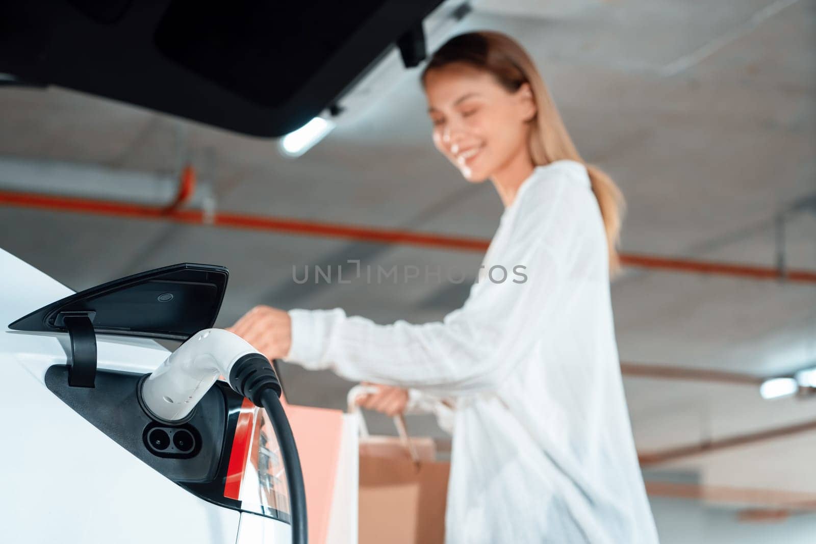 Young woman travel with EV electric car to shopping center parking lot innards by biancoblue