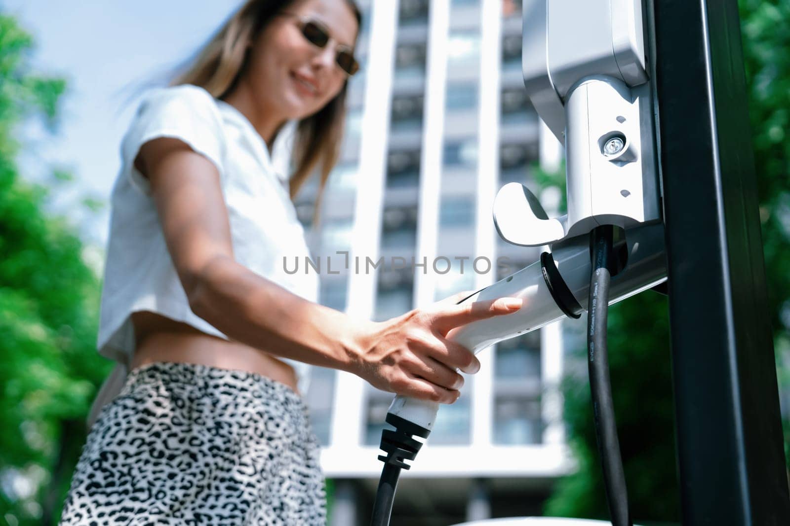 Young woman travel with EV electric car in green sustainable city innards by biancoblue