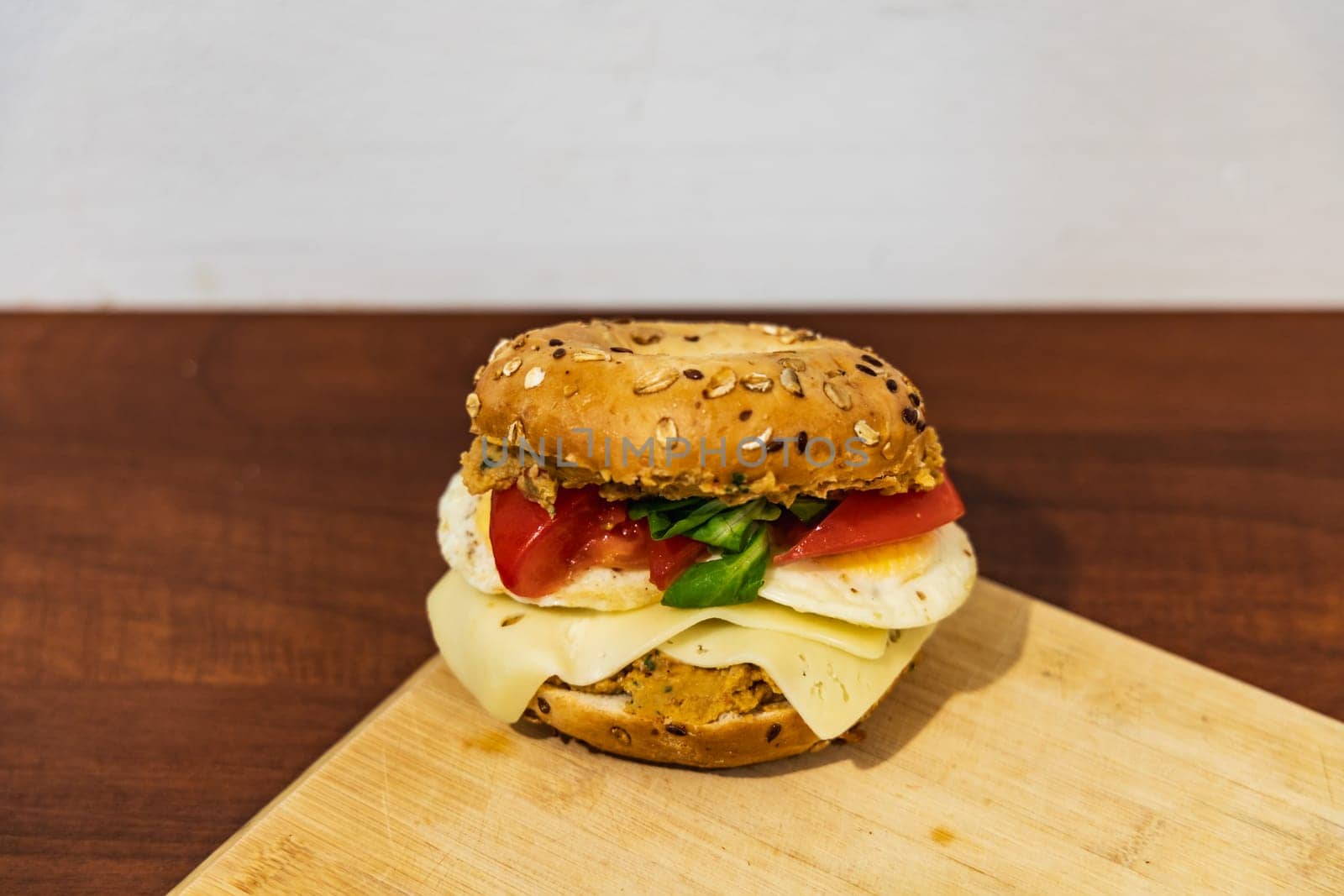 Fresh breakfast bagel bun with seeds with hummus and cheese eggs tomato and salad lying on wooden board by Wierzchu