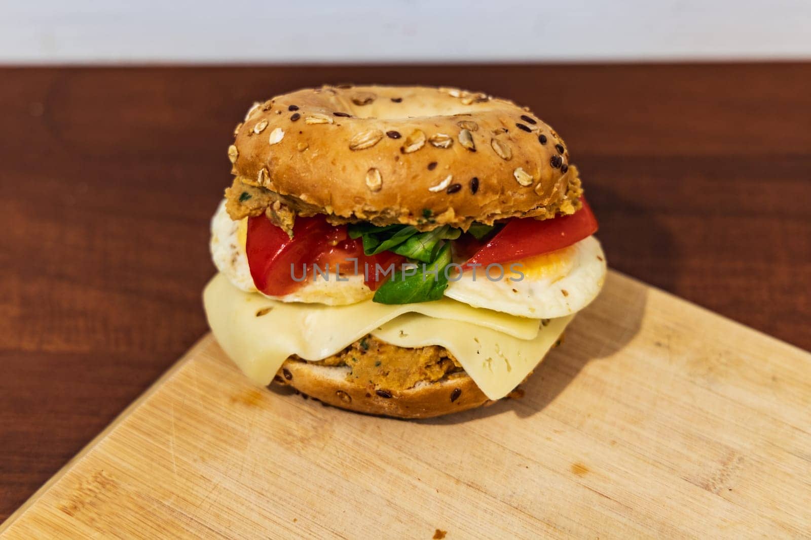 Fresh breakfast bagel bun with seeds with hummus and cheese eggs tomato and salad lying on wooden board by Wierzchu