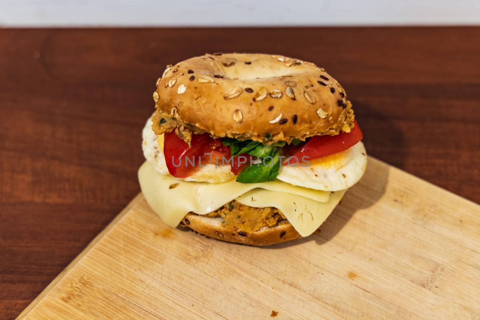 Fresh breakfast bagel bun with seeds with hummus and cheese eggs tomato and salad lying on wooden board by Wierzchu