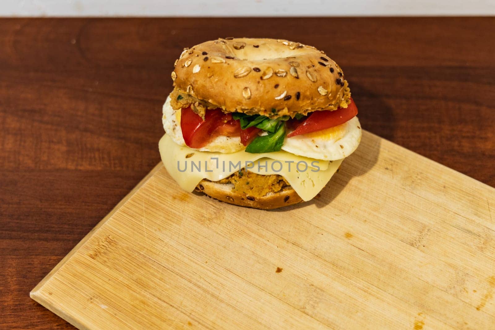 Fresh breakfast bagel bun with seeds with hummus and cheese eggs tomato and salad lying on wooden board