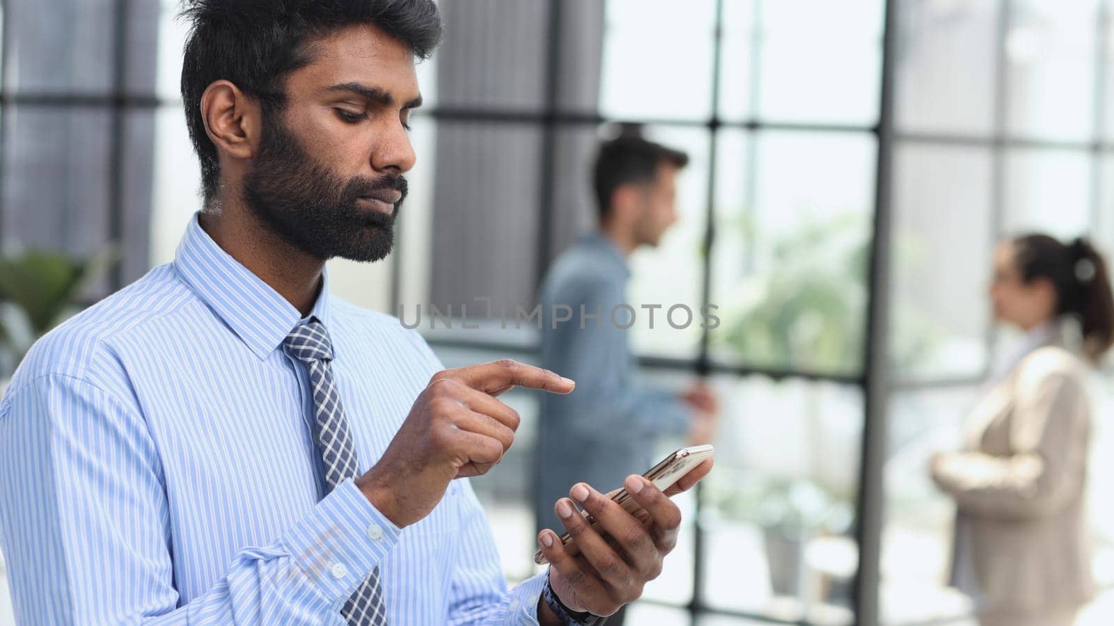 A young stands inside office, the man holds the phone in his hands, the businessman browses online pages and uses applications