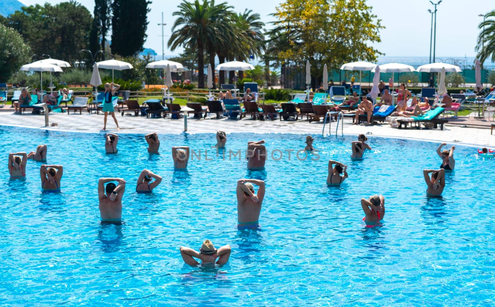 BUDVA, MONTENEGRO - SEPTEMBER 08, 2023: Enthusiastic group engaged in aqua aerobics at a hotel's outdoor pool. Concept of fitness and fun in water by Mariakray