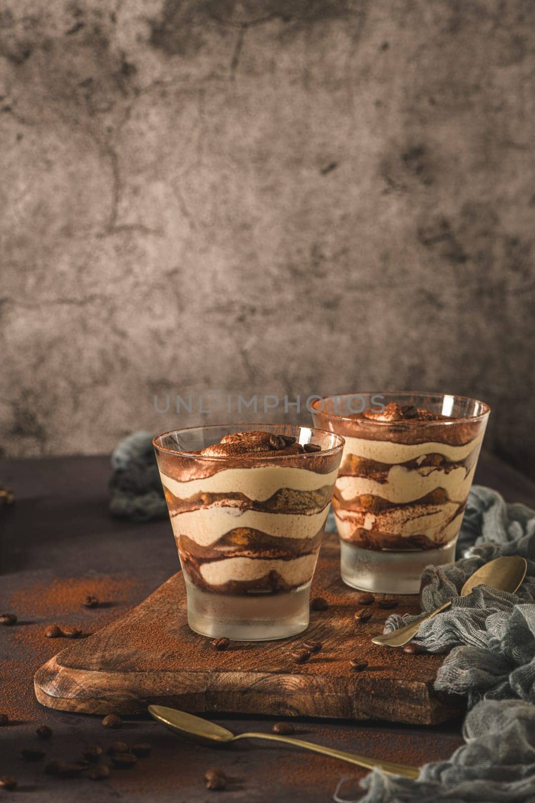 Delicious italian dessert tiramisu in a glasses on a dark slate, stone or concrete background.