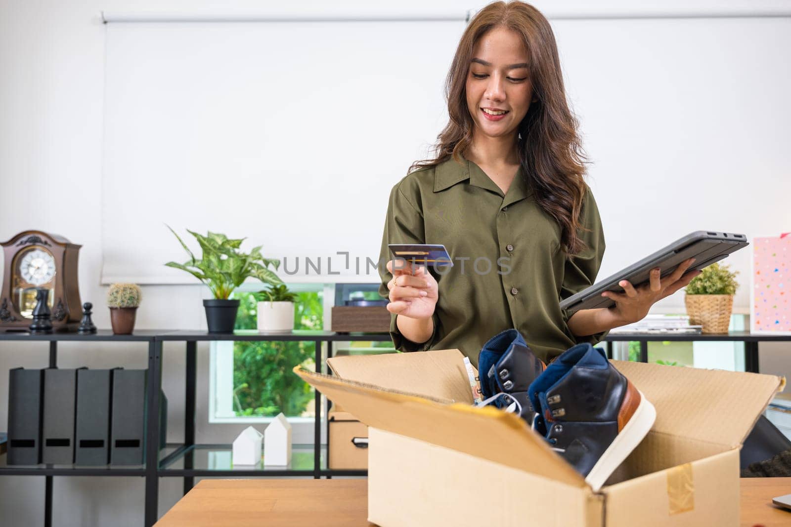 Asian young woman received online shopping parcel opening shoes boxes to checking on digital tablet, Cheerful woman holding credit card, happy female unpacking cardboard box, Shop online and delivery