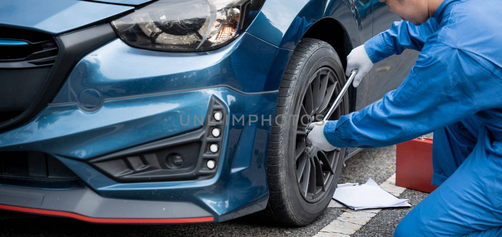 Close-up of a young mechanic's hand in a blue work uniform, fixing a tire. Cropped shot.