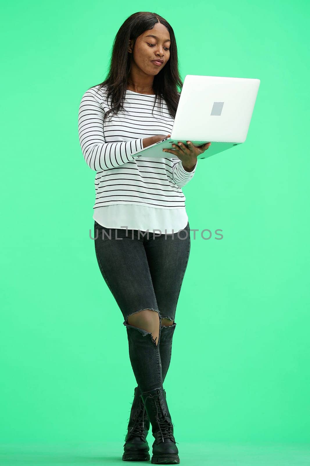 A woman, on a green background, in full height, uses a laptop by Prosto