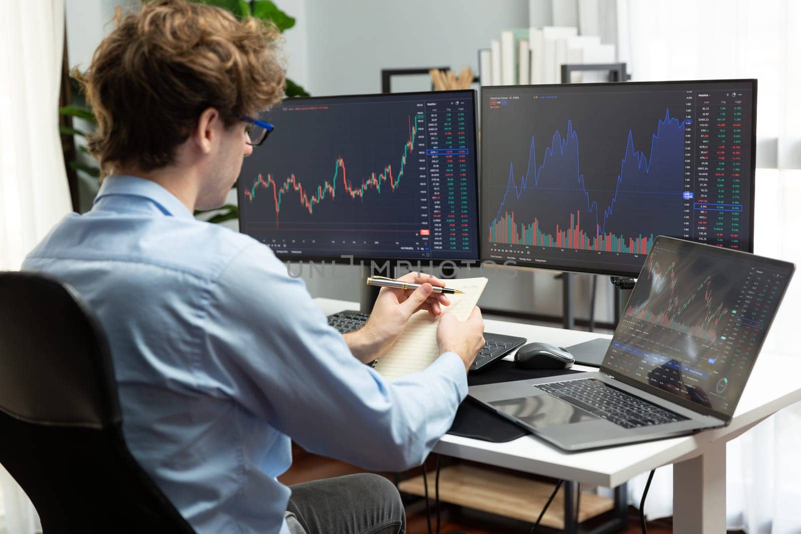 Working young business trader looking on laptop on screens, holding notepad and pen on market stock graph investing in real time at office on panorama, analyzing dynamic investment concept. Gusher.