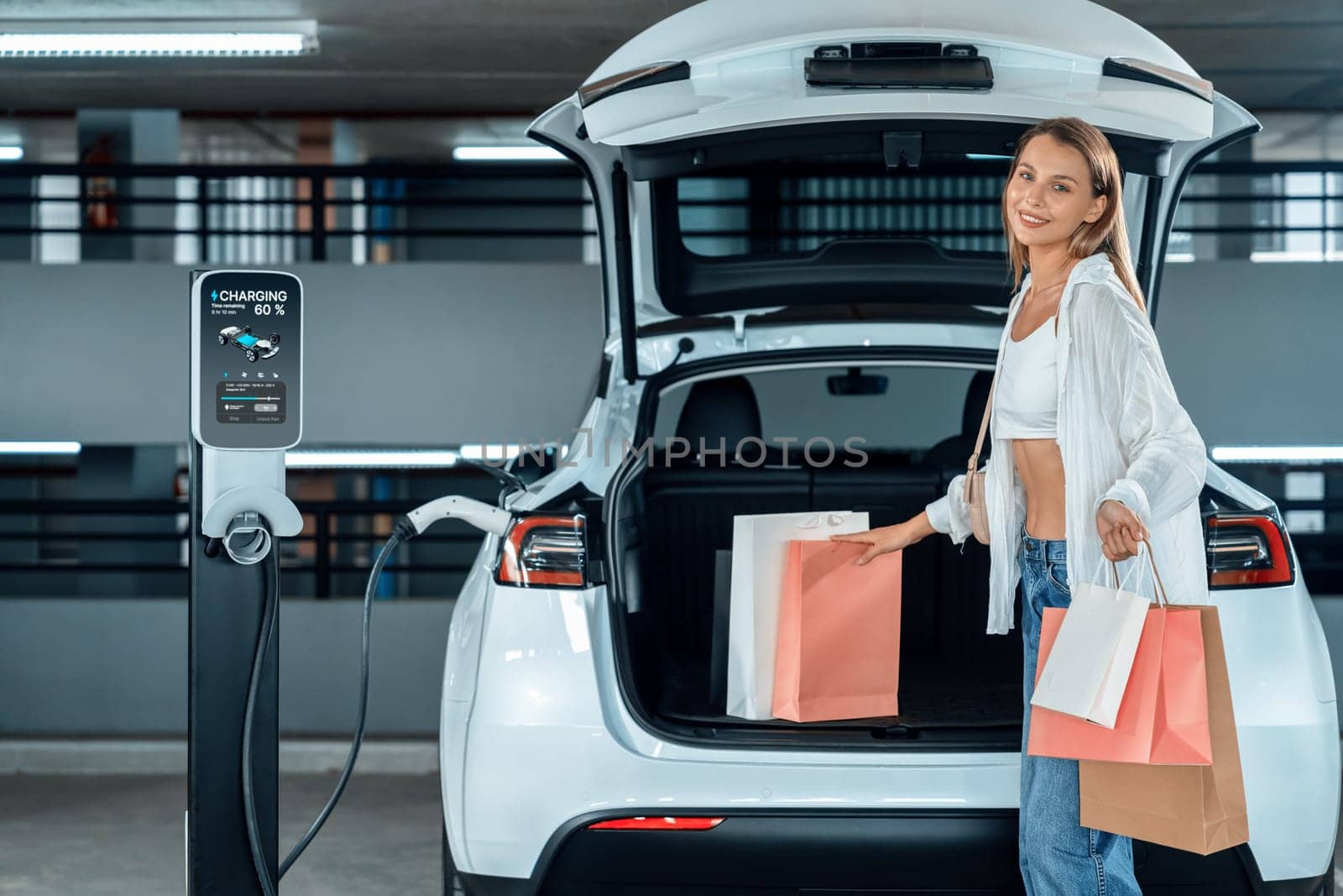 Young woman travel with EV electric car to shopping center parking lot innards by biancoblue