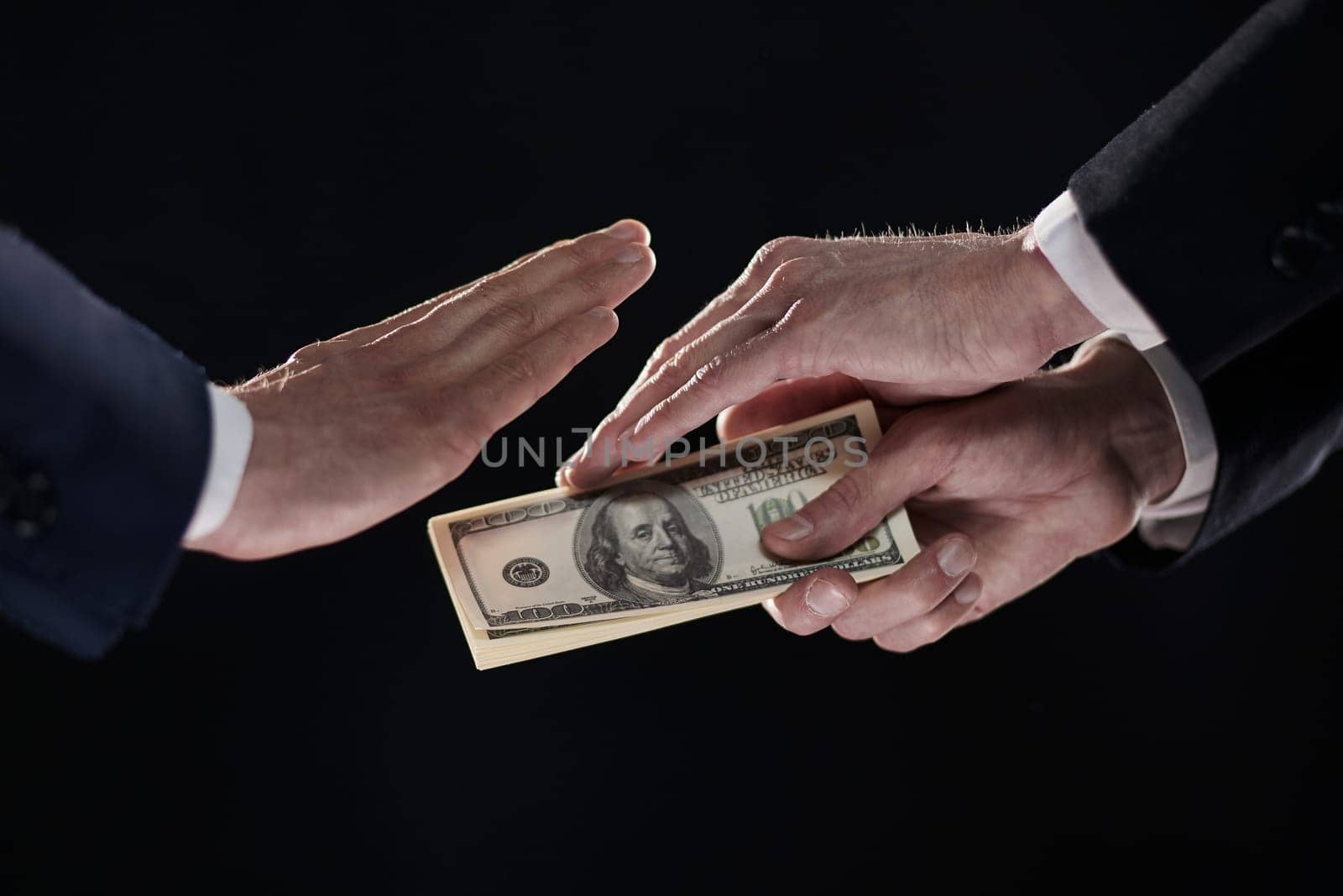 A man's hand in a black suit holds out a wad of money, which refuses. On a black background