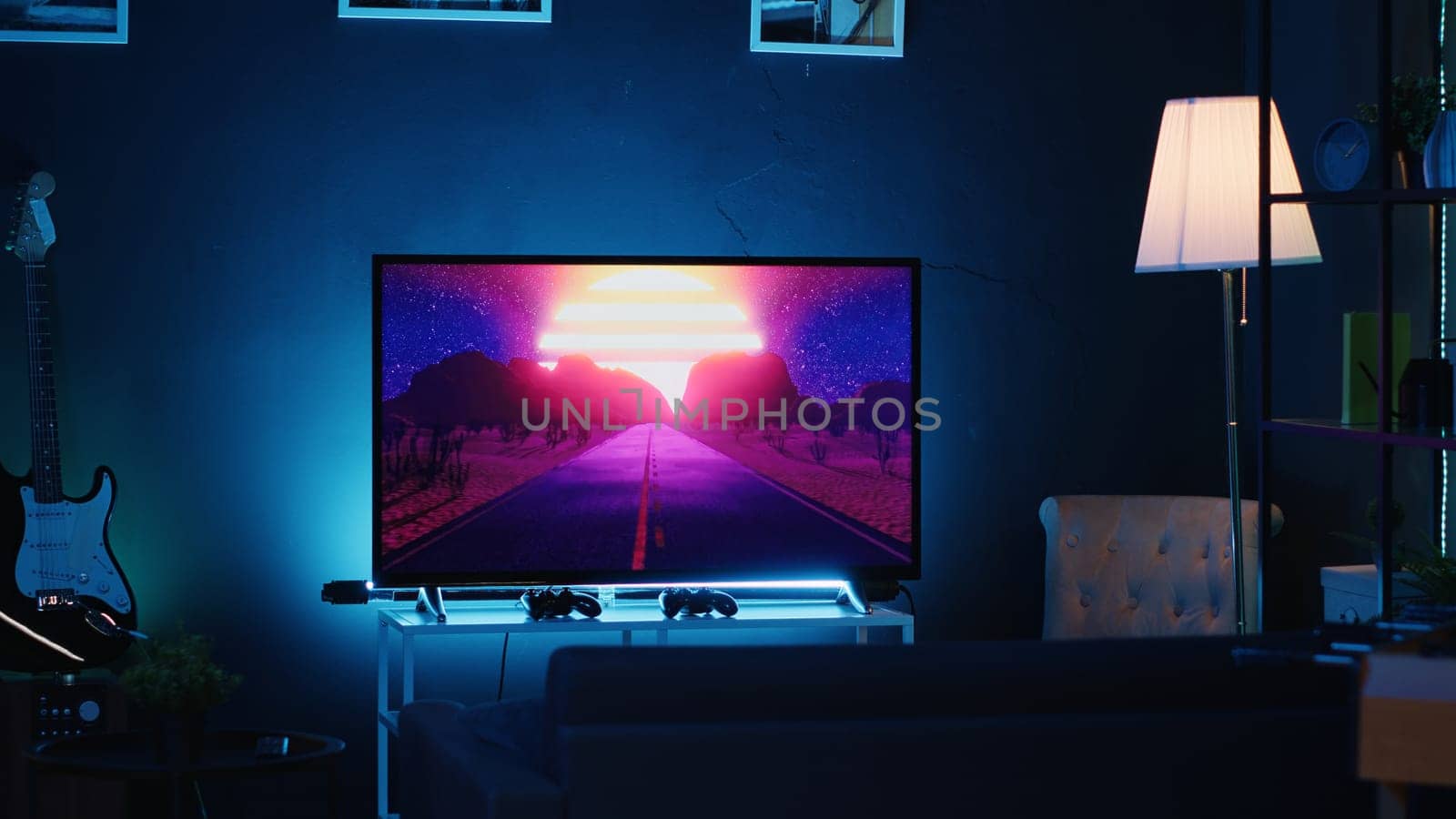 Empty stylish neon lit home studio interior illuminated with neon lights at night and artwork decorating the walls. Modern apartment with TV running in background on news channel broadcast