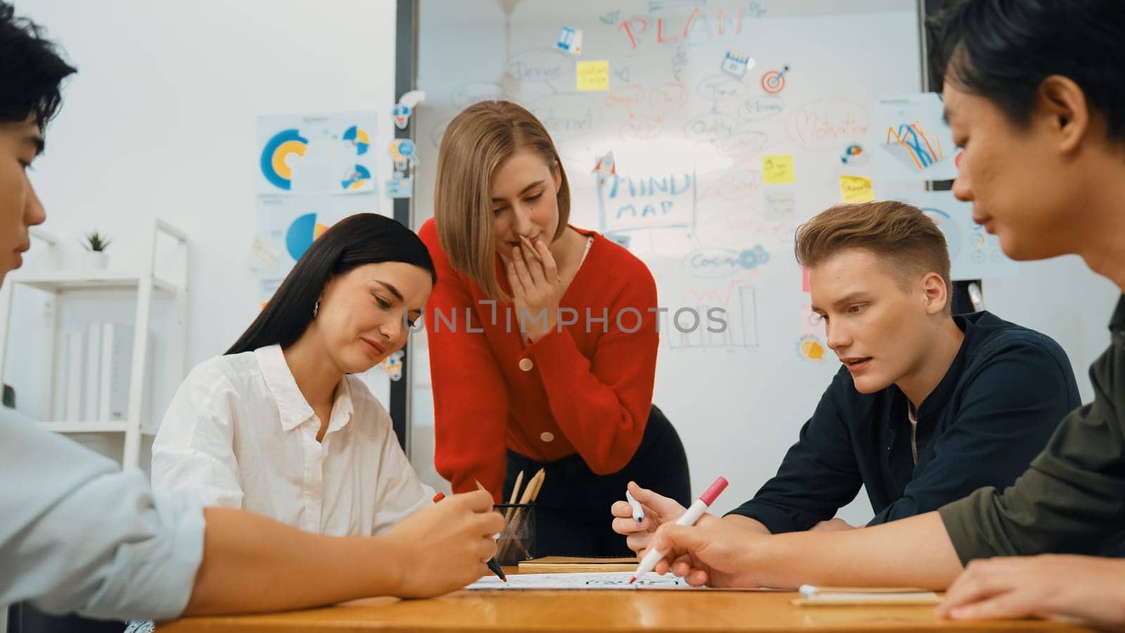 Creative happy business team brainstorming and sharing idea by using mind map and graphic graph while young beautiful project manager pointing at important point at business meeting. Immaculate.