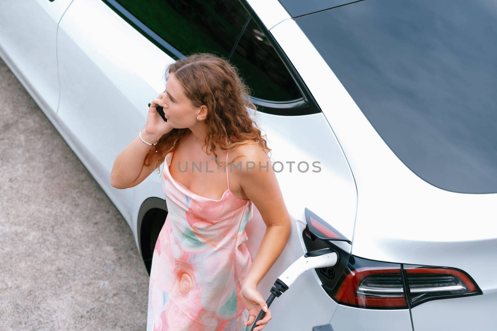 Modern eco woman recharge EV car with smartphone. Synchronos by biancoblue