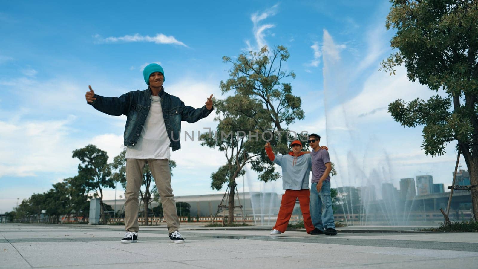 Professional attractive hipster perform street dance with fountain. Panorama shot of attractive handsome man practice b-boy footstep. Blue background. Modern lifestyle. Outdoor sport 2024. Sprightly.