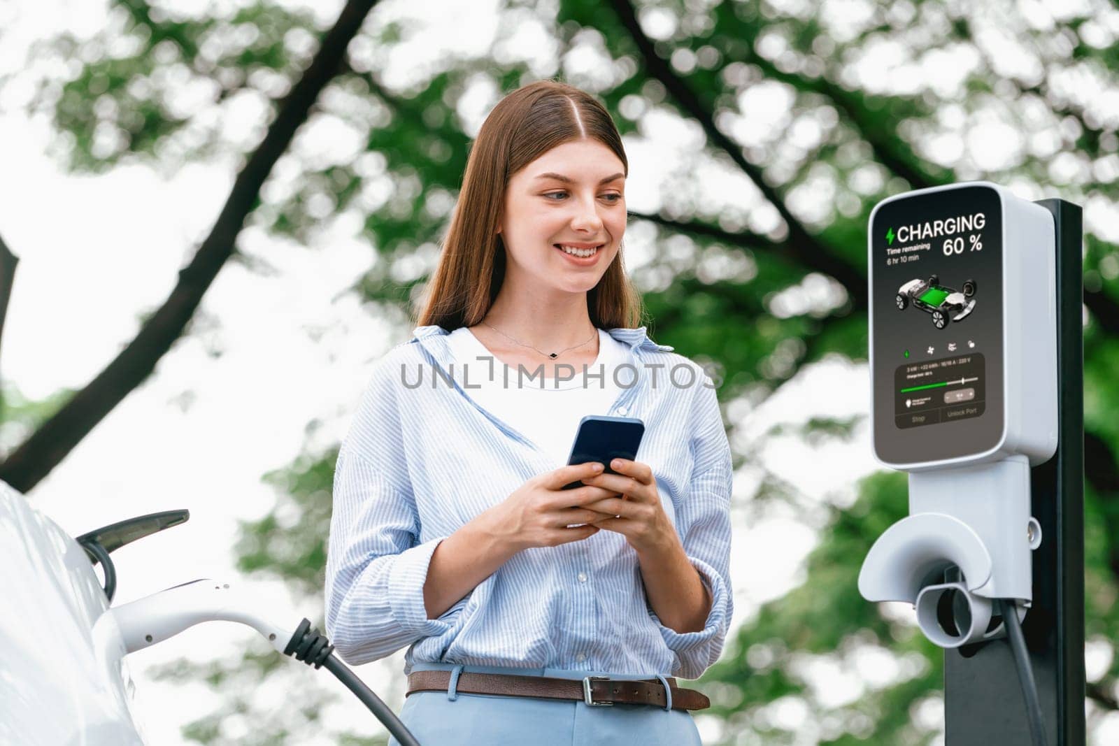 Young woman using smartphone to pay for electric car charging. Exalt by biancoblue