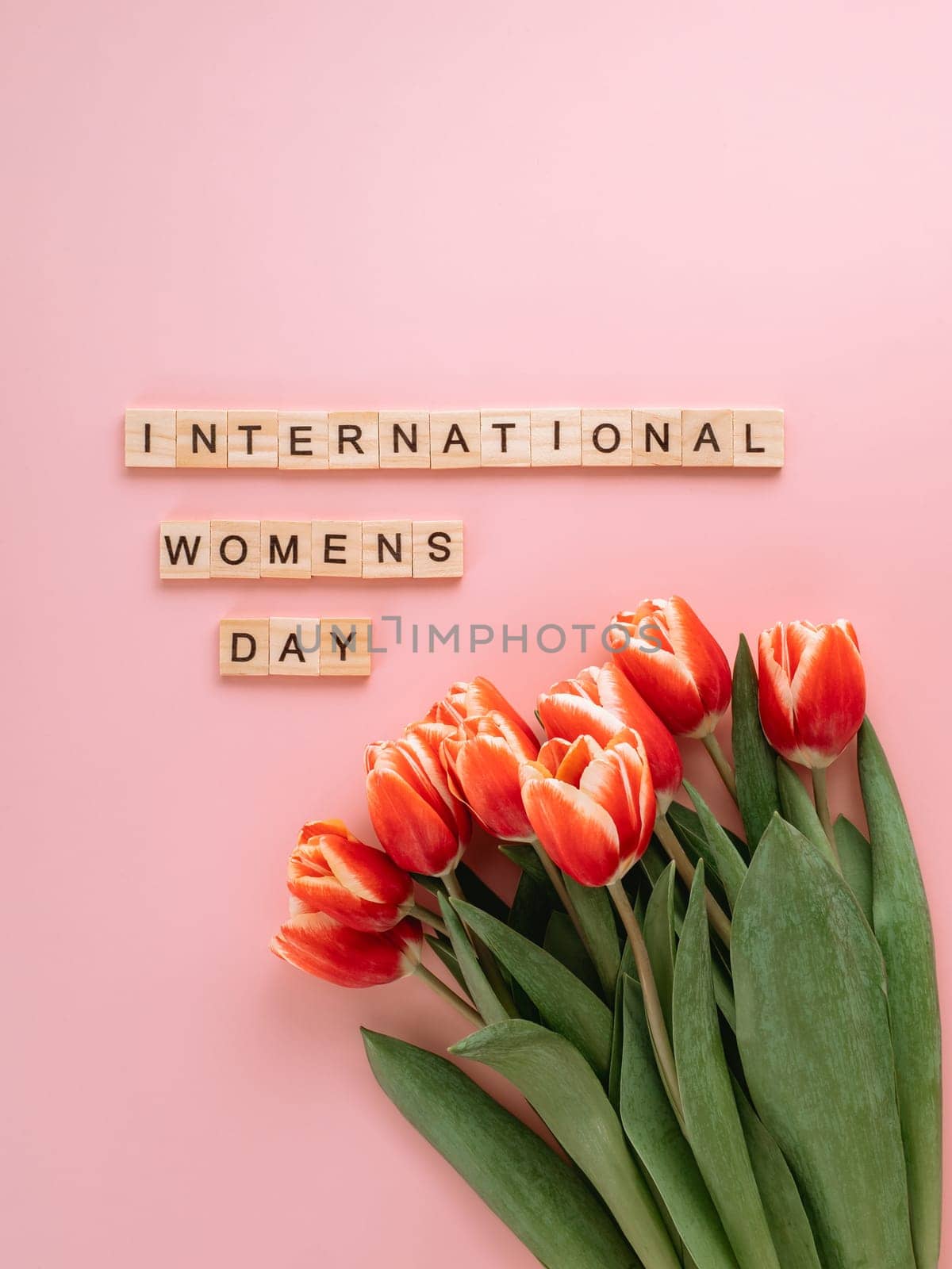 International women's day or eight march concept with copy space. International women's day text and bunch of red tulip on pink background. Top view or flat lay. Vertical