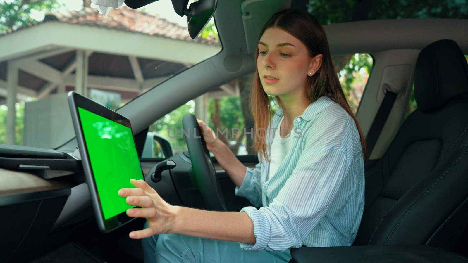 Holiday vacation road trip with environmental-friendly car concept. Eco-conscious young couple on driver seat holding blank copyspace green screen car's monitor for EV battery status. Exalt