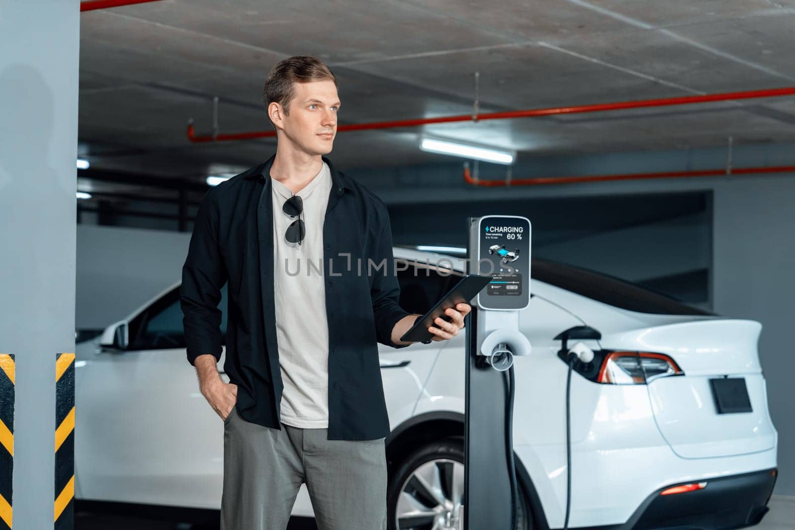 Young man travel with EV electric car to shopping center parking lot charging in downtown city showing urban sustainability lifestyle by green clean rechargeable energy of electric vehicle innards