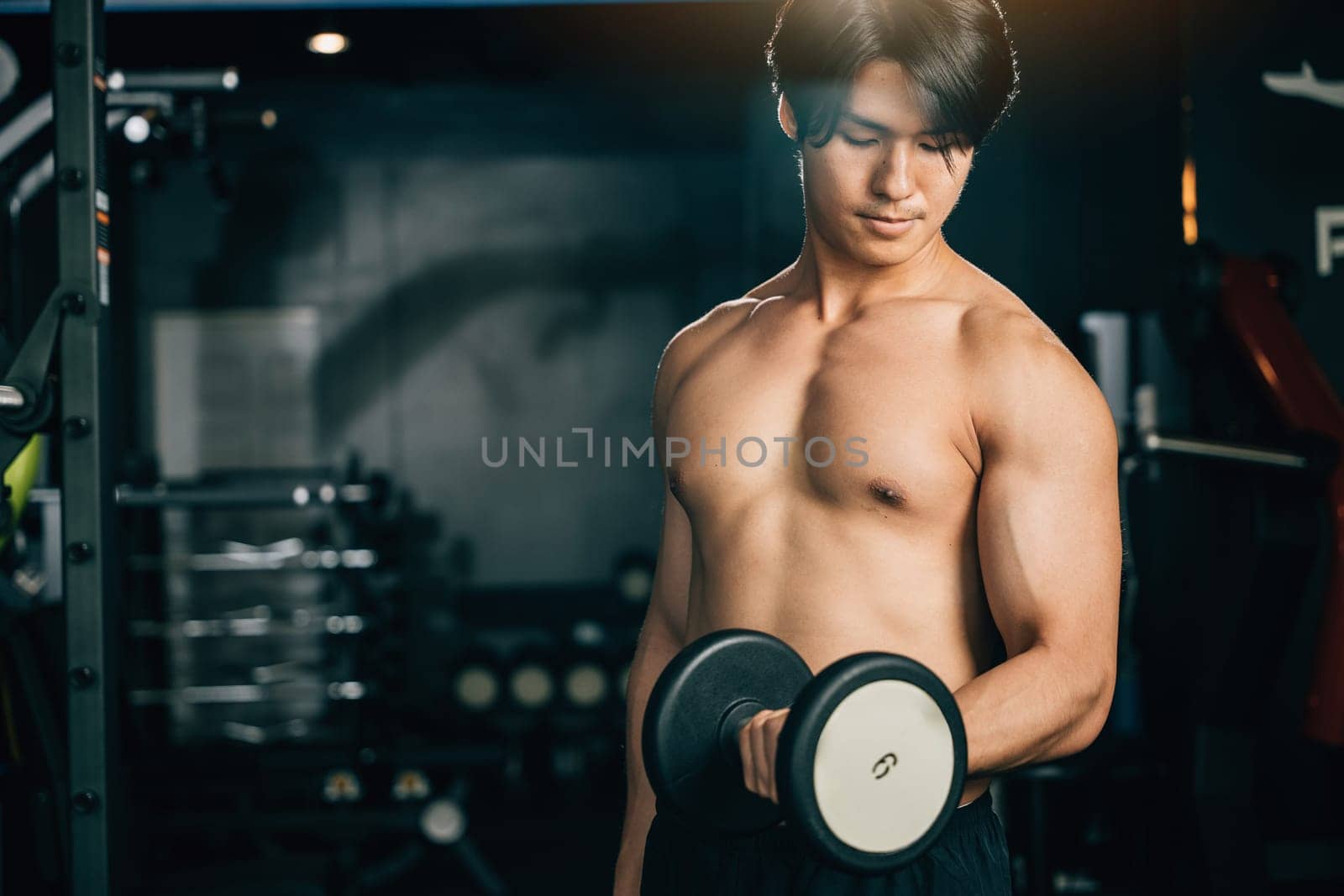 A man in black workout clothes, his hands gripping heavy dumbbells, exerts effort and determination to lift weights and build his muscle shape. Fitness GYM Healthy sports lifestyle concept