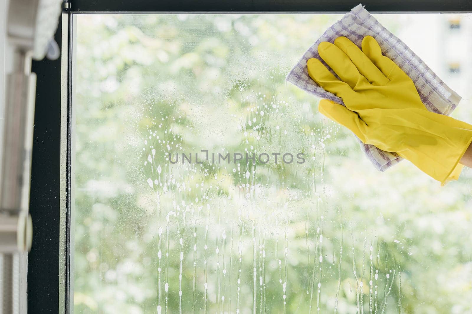 With happiness a young woman maid sprays and wipes office windows. Her housework routine emphasizes purity hygiene and transparent cleanliness for sparkling windows. by Sorapop