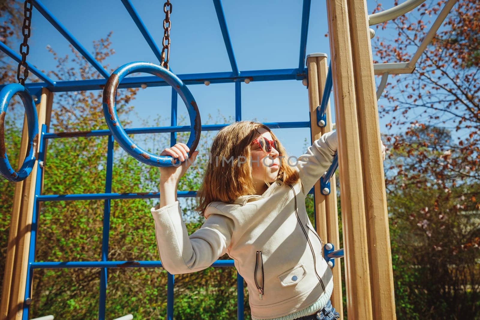 Cute preschooler girl climbing on a playground equipment on the blue sky background. happy girl in beige jacket