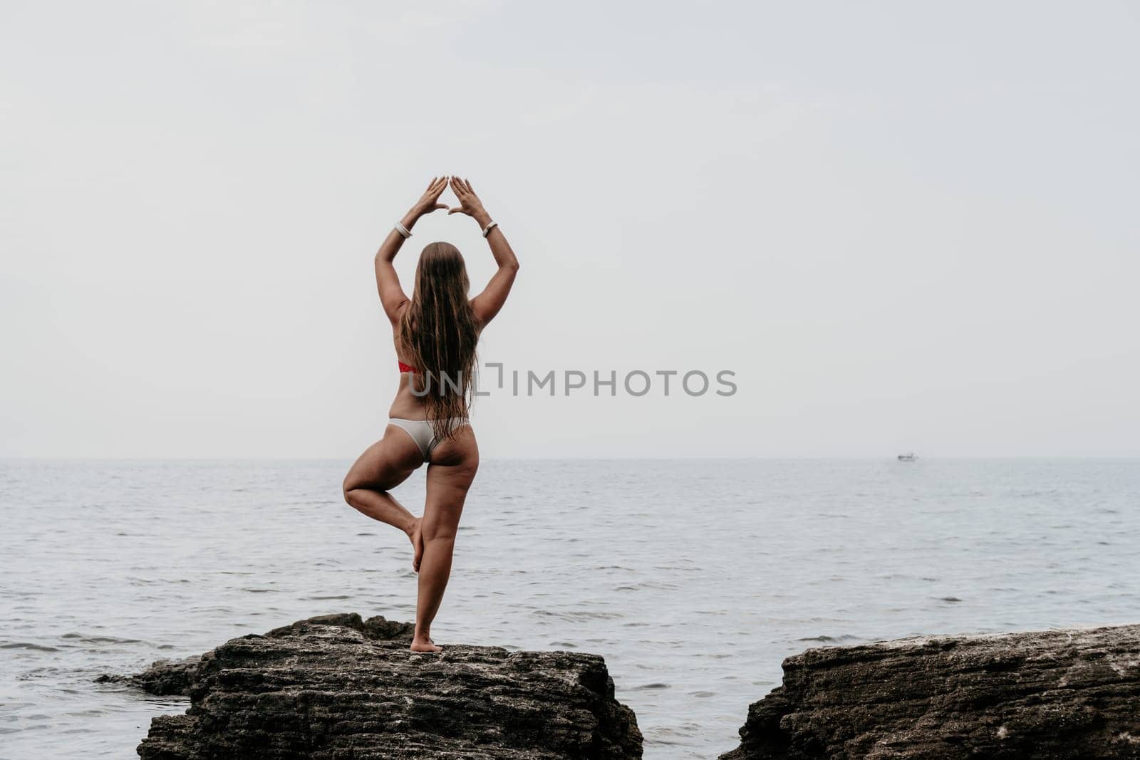 Woman sea yoga. Back view of free calm bliss satisfied woman with long hair standing on top rock with yoga position against of sky by the sea. Healthy lifestyle outdoors in nature, fitness concept. by panophotograph