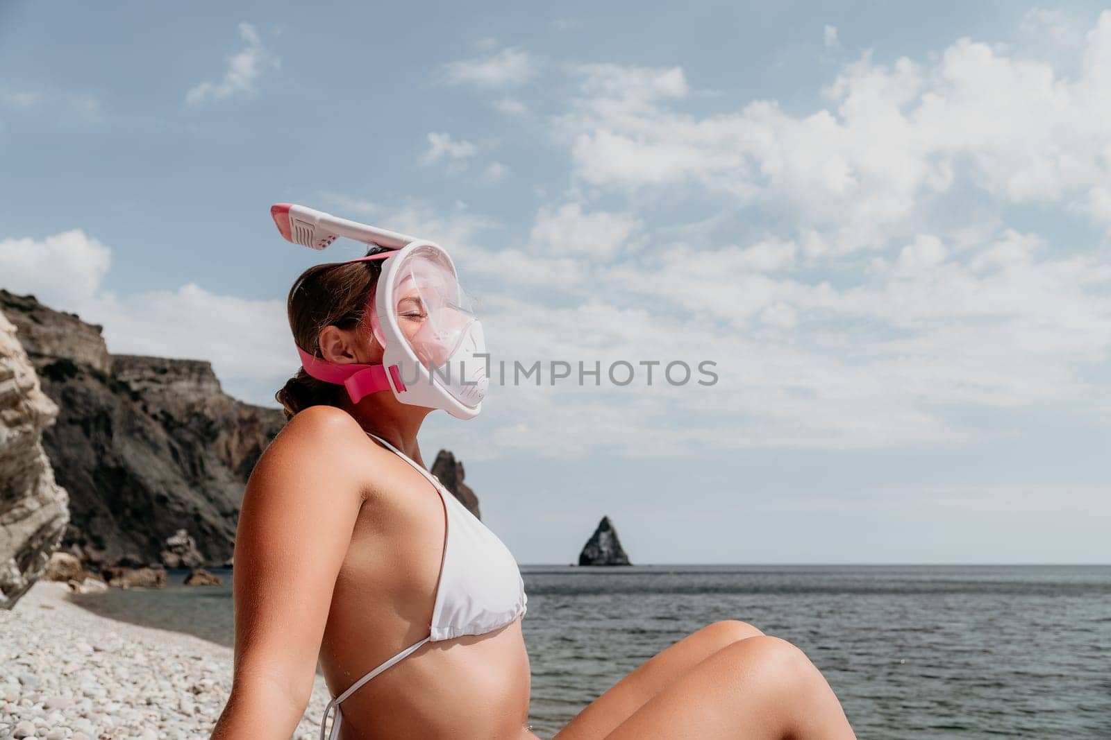 Young happy woman in white bikini put pink snorkeling mask on beach before swimming. girl having fun relaxing on beautiful beach. Beach lifestyle