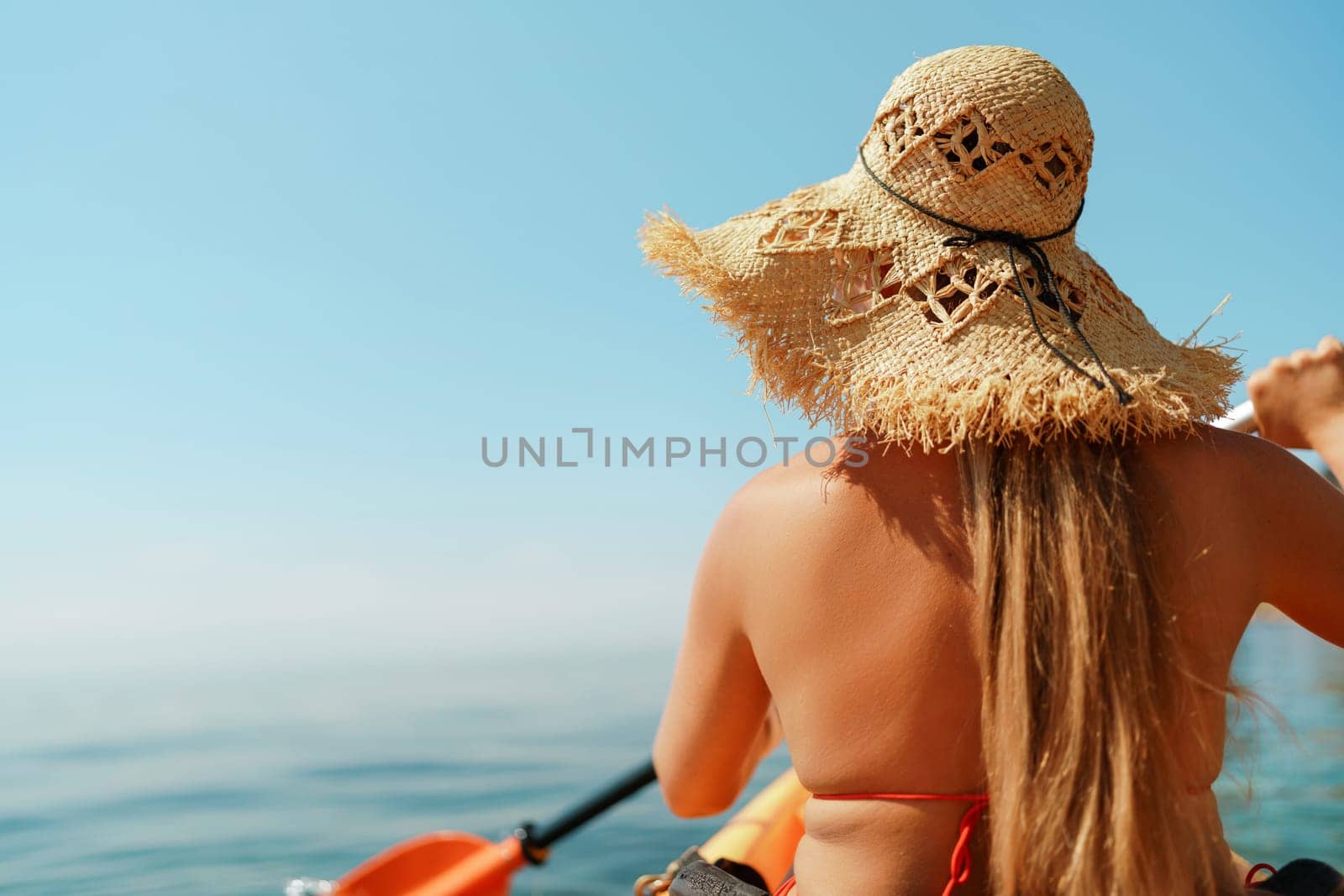 Woman in kayak back view. Happy woman with long hair in a swimsuit and hat floating in kayak on the sea. Summer holiday vacation. Summer holidays vacation at sea