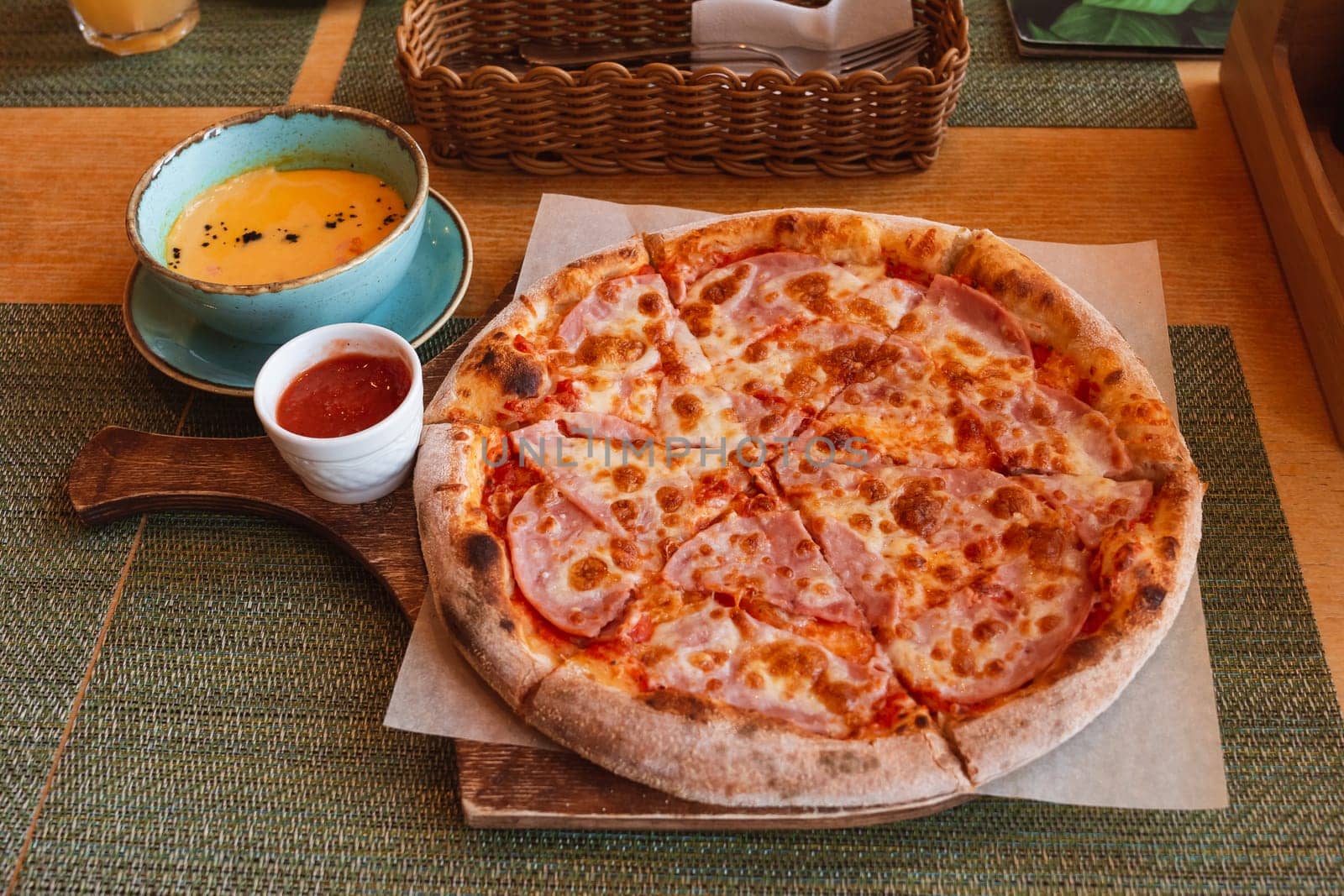 Pizza with ham cut into pieces, lying on the board. Pumpkin cream soup with salmon