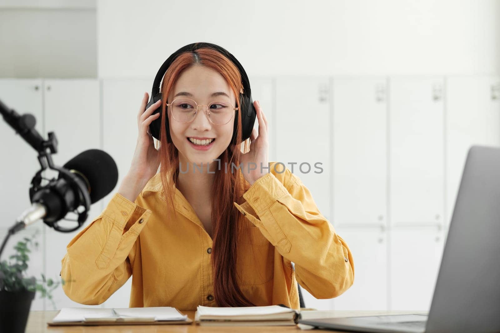 Cheerful woman hosting a live podcast, engaging with audience using professional microphone in studio.