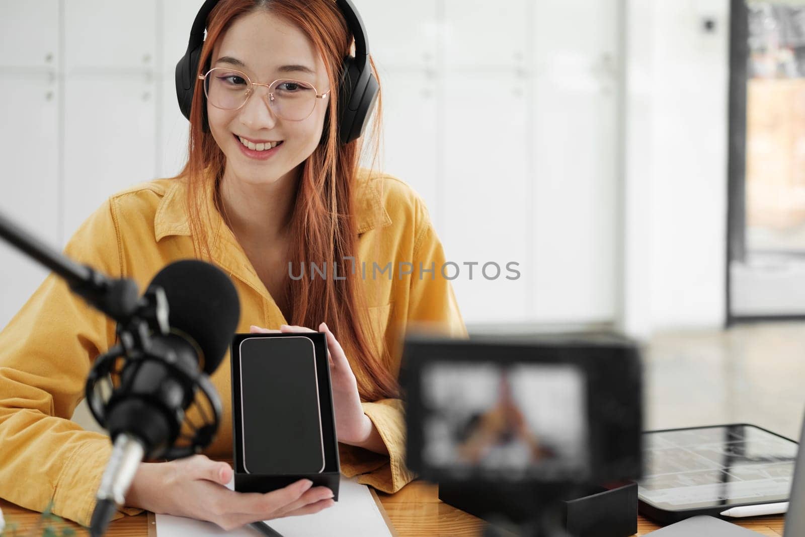 Woman recording a podcast on her laptop computer with headphones and a microscope. Female podcaster making audio podcast from her home studio.