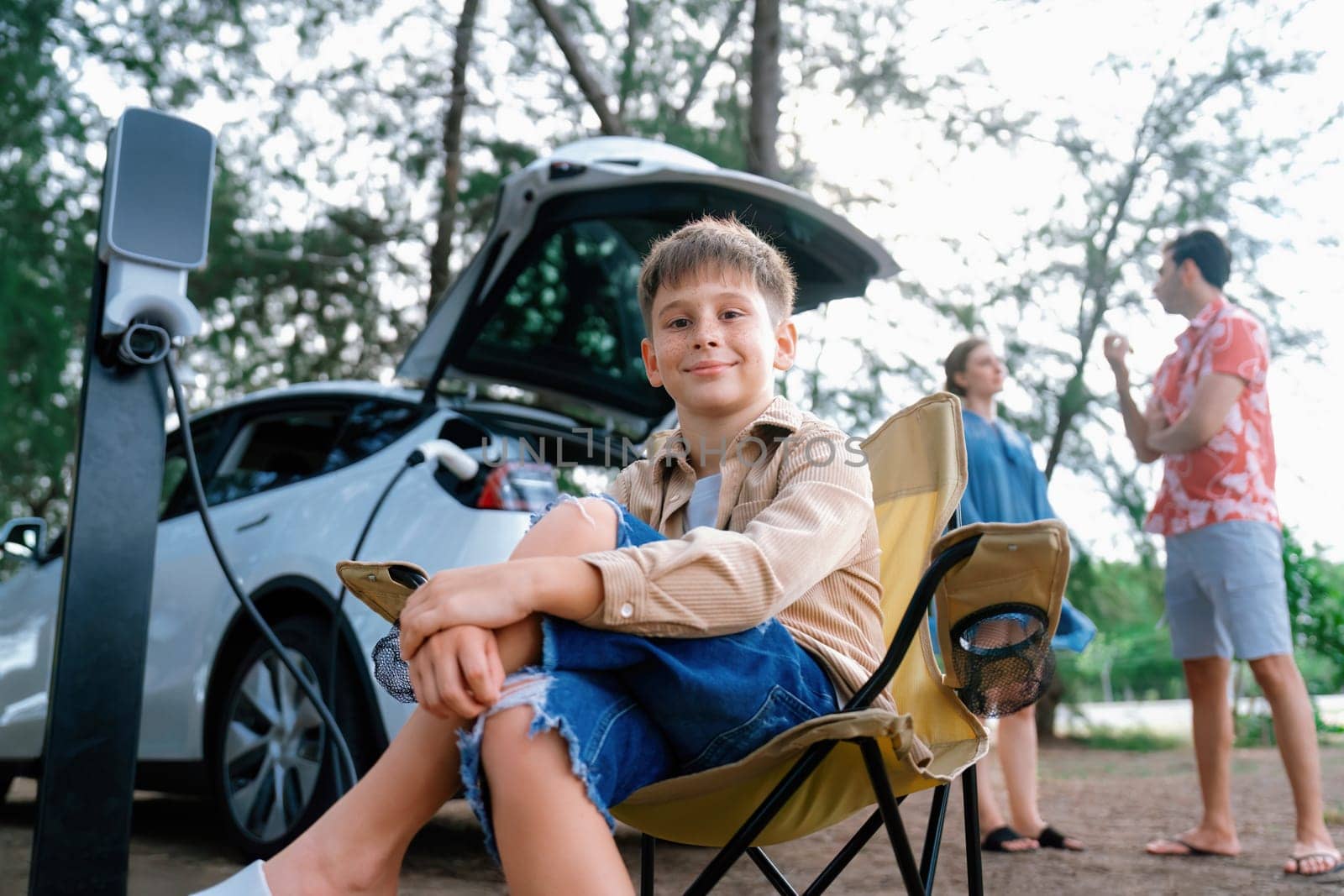 Little boy portrait sitting on camping chair with family. Perpetual by biancoblue