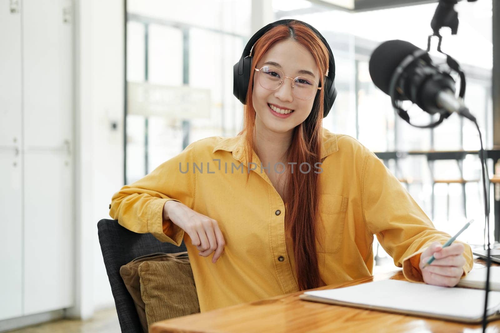 Woman recording a podcast on her laptop computer with headphones and a microscope. Female podcaster making audio podcast from her home studio.