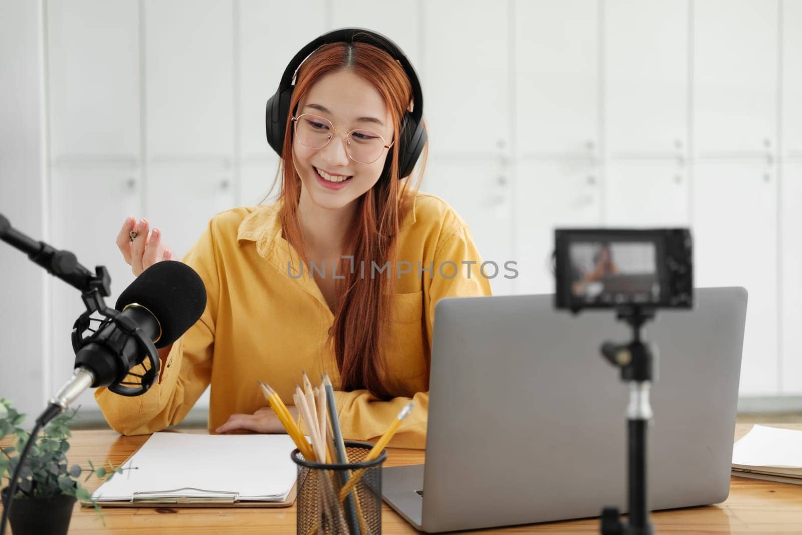 Cheerful woman hosting a live podcast, engaging with audience using professional microphone in studio.