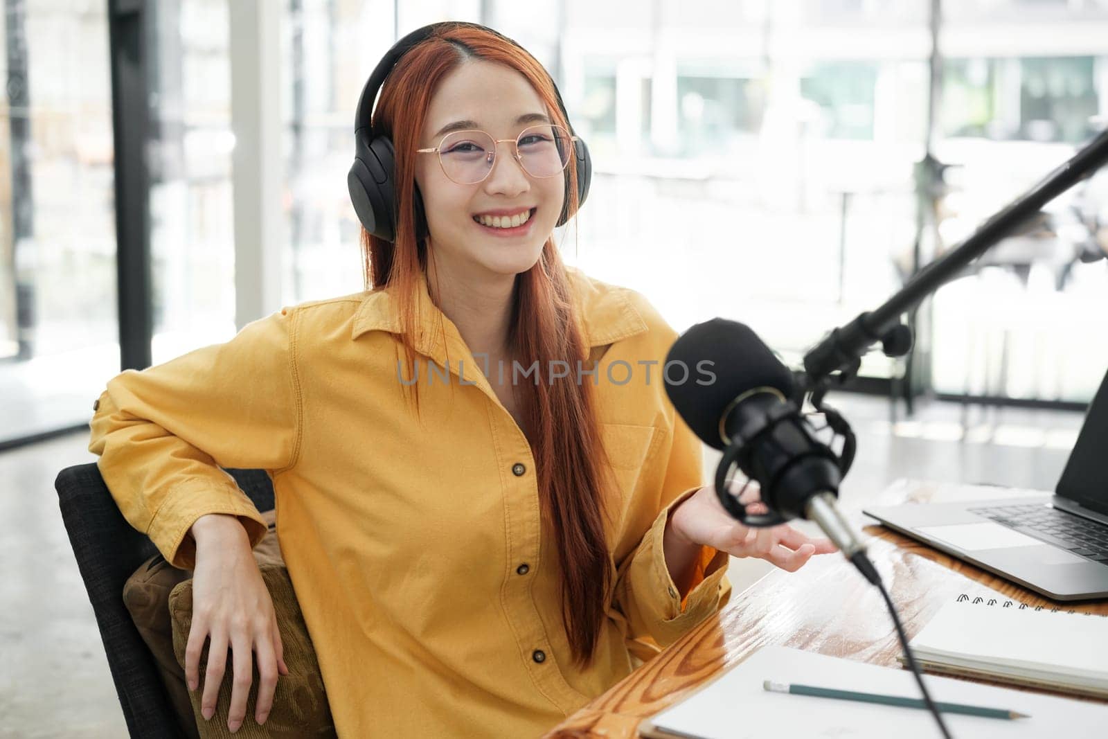 Cheerful woman hosting a live podcast, engaging with audience using professional microphone in studio.