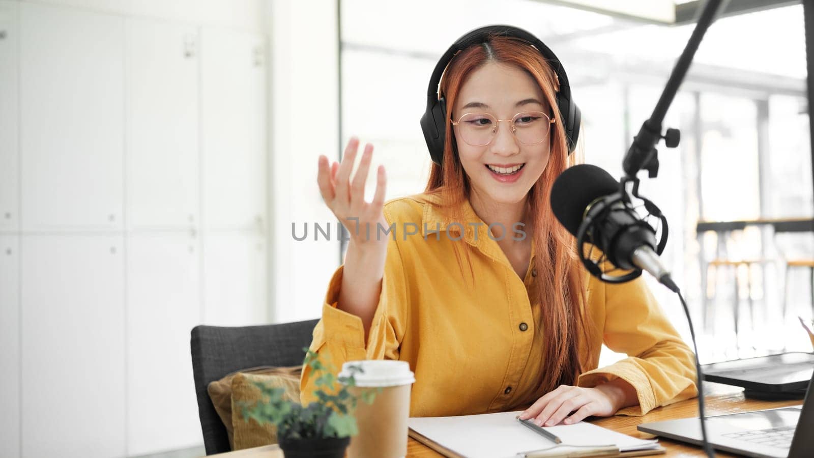 Cheerful woman hosting a live podcast, engaging with audience using professional microphone in studio.