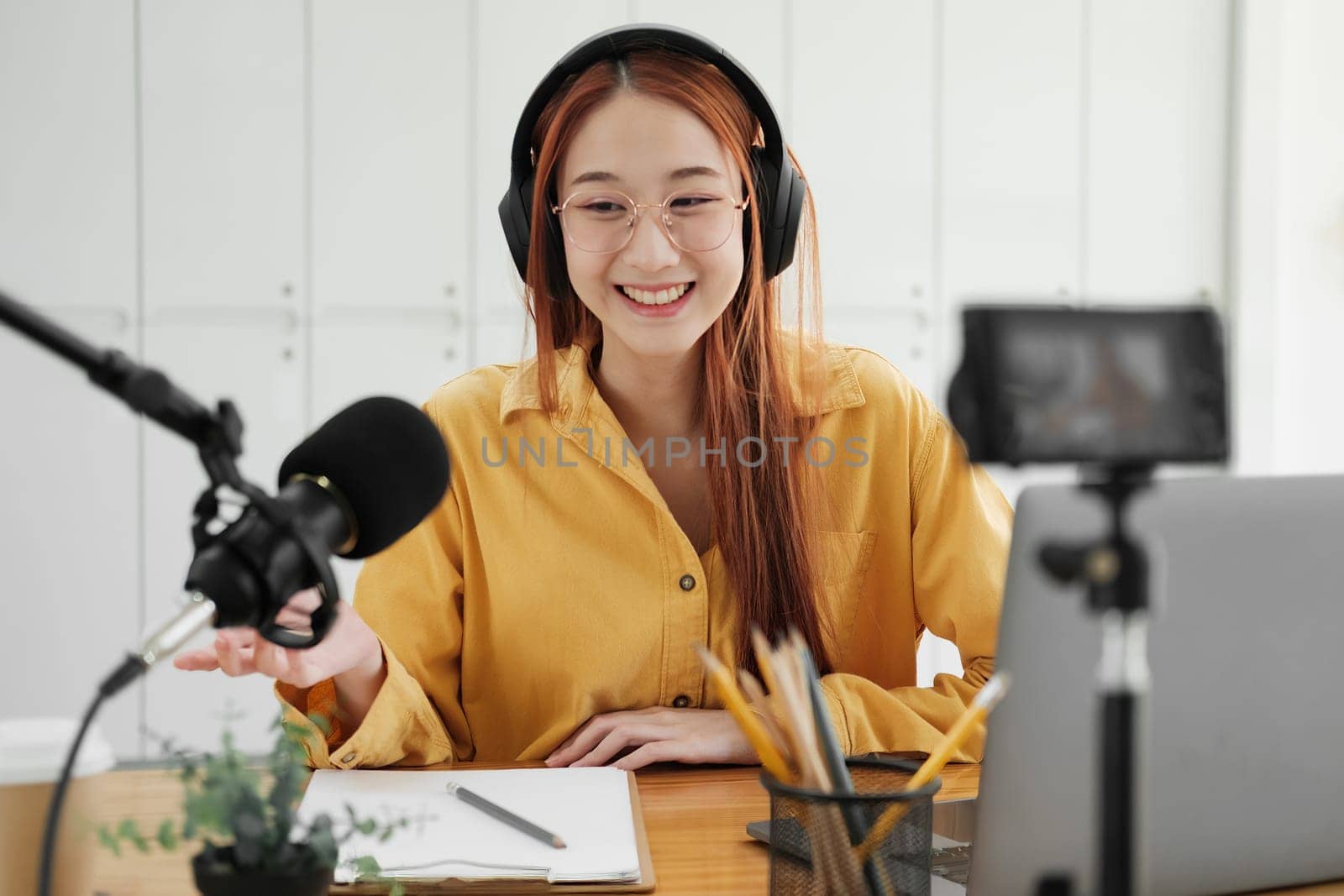 Cheerful woman hosting a live podcast, engaging with audience using professional microphone in studio.