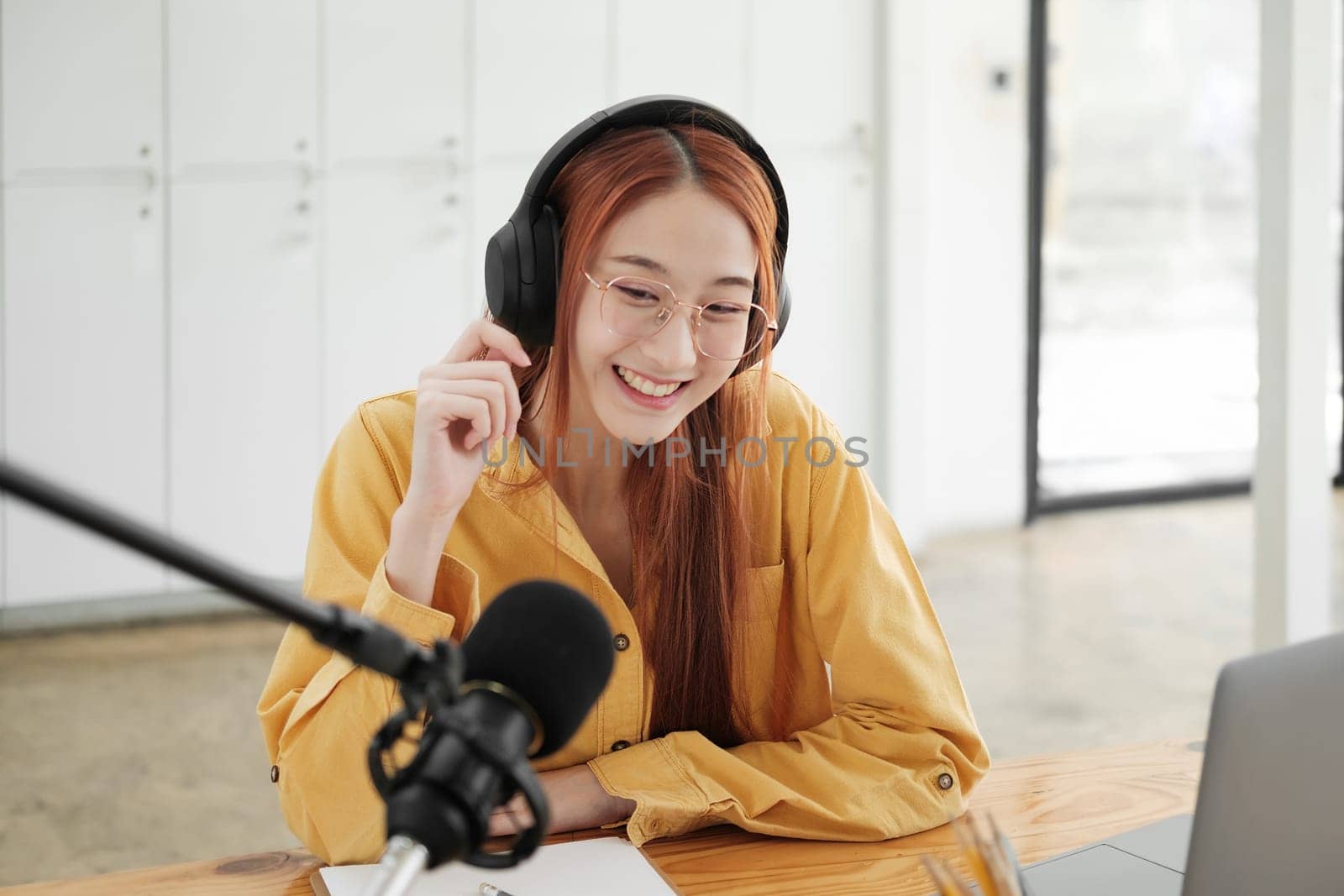 Cheerful woman hosting a live podcast, engaging with audience using professional microphone in studio.