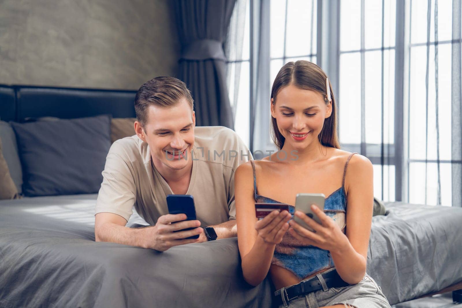 Young couple sit in the bed room using online payment app. Unveiling by biancoblue