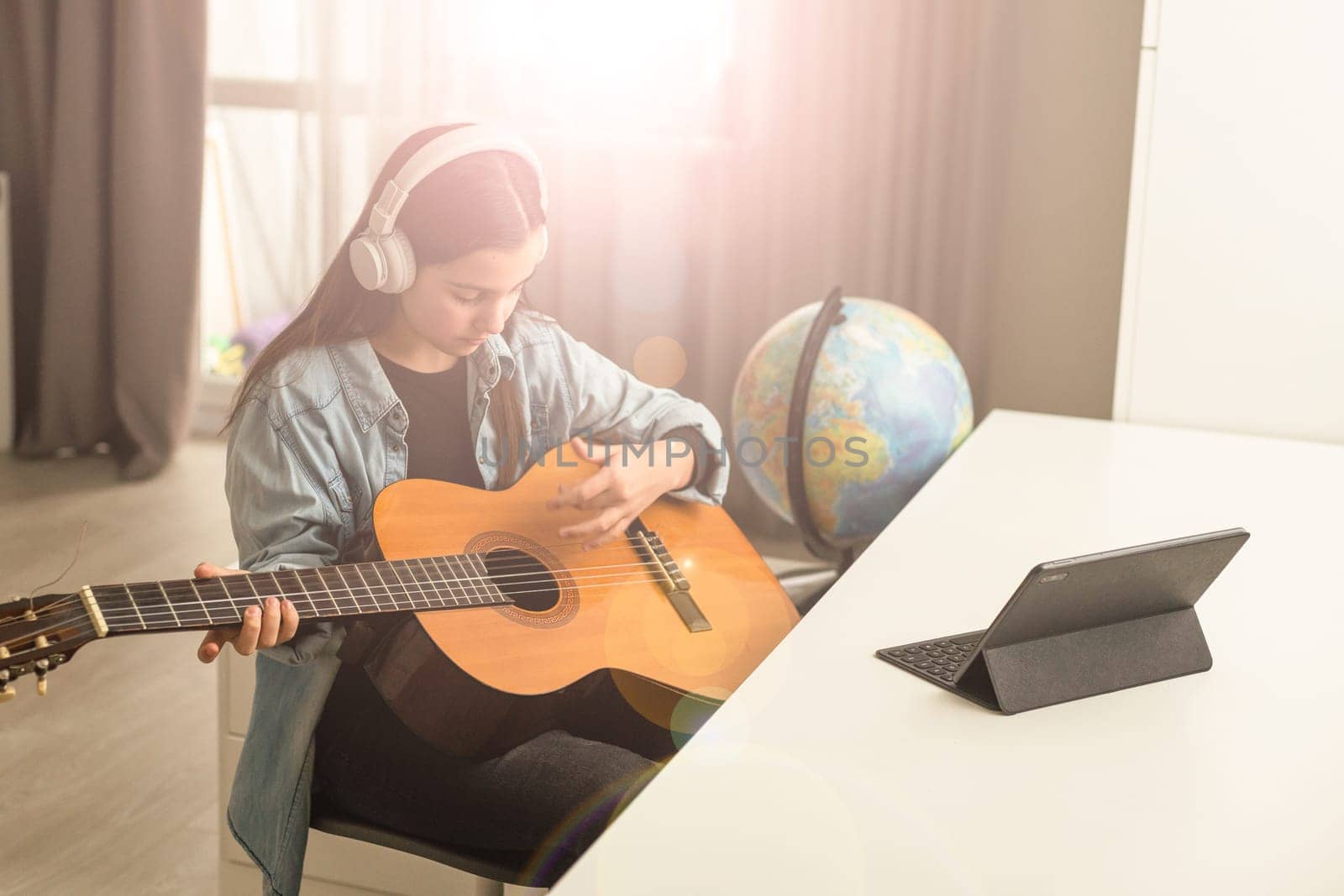 Teenager girl learning to play guitar at home using online lessons. Hobby remote musical education acoustic guitar. Copy space. High quality photo
