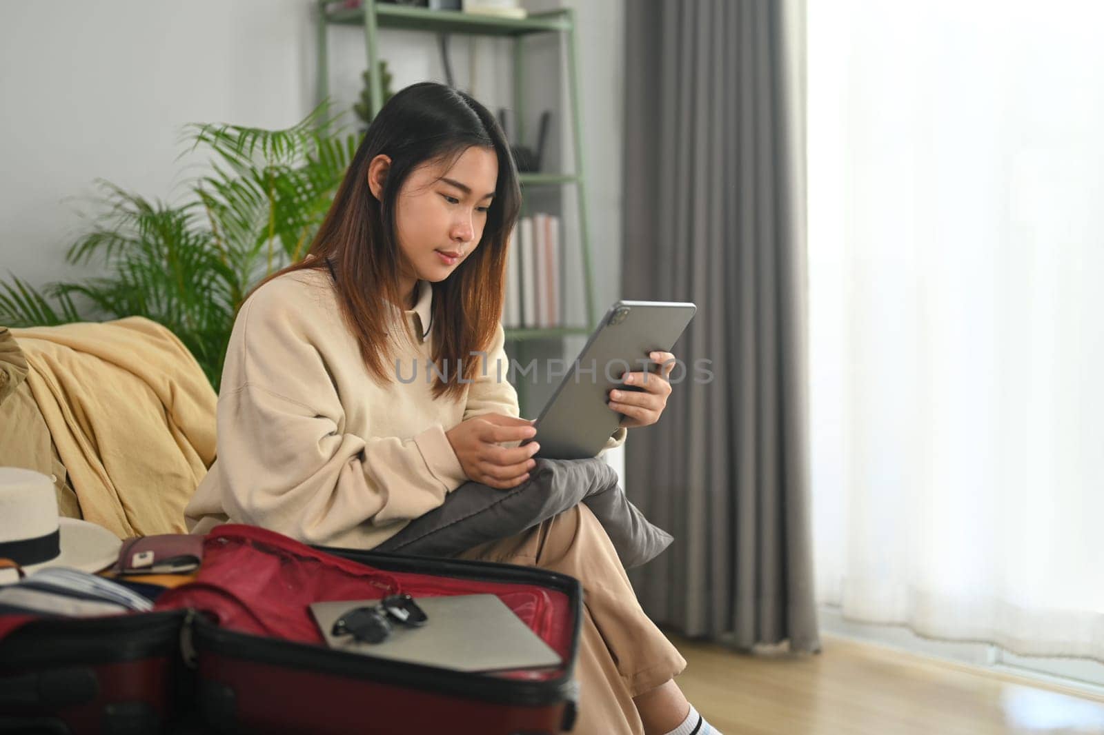 Young woman sitting on sofa searching for lodging using online web service on digital tablet by prathanchorruangsak