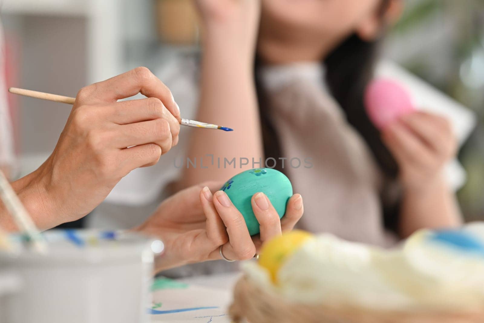 Closeup mother and her daughter painting easter eggs in living room, getting ready for holiday by prathanchorruangsak