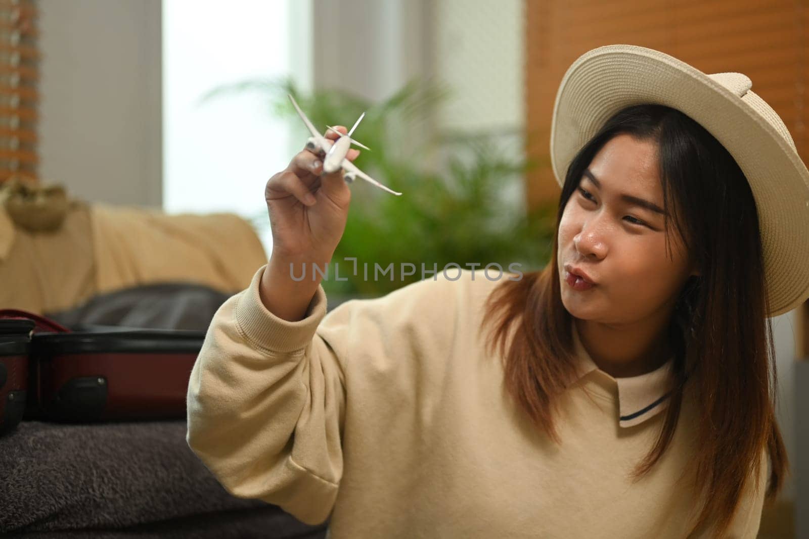 Cheerful young woman holding airplane model, sitting near unpacked suitcases. Traveling, vacation and transportation concept.