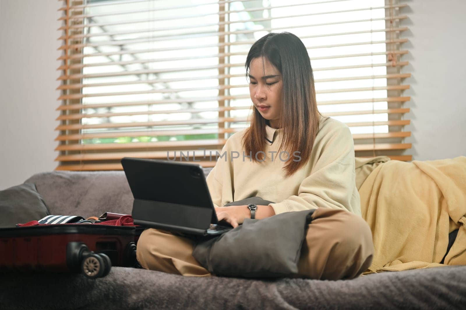 Smiling young woman using laptop for choosing travel destination for trip or booking hotel online.